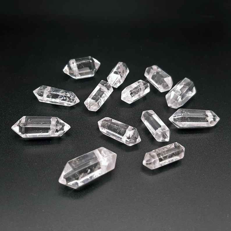 May include: A collection of clear quartz crystal points, also known as double terminated quartz crystals, arranged on a black surface. The crystals are faceted and have a natural, raw appearance.