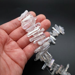 Pode incluir: Um fio de pontas de cristal de quartzo claro iridescente, tamb&eacute;m conhecido como quartzo aura de anjo, enfiado em um fio branco. Os cristais s&atilde;o de v&aacute;rios tamanhos e formas, alguns s&atilde;o mais longos e finos que outros.