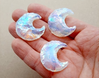 May include: Three iridescent white crescent moon shaped stones. The stones are smooth and have a pearlescent finish.