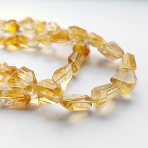 May include: A strand of faceted citrine beads in a warm yellow color. The beads are faceted and have a translucent appearance.