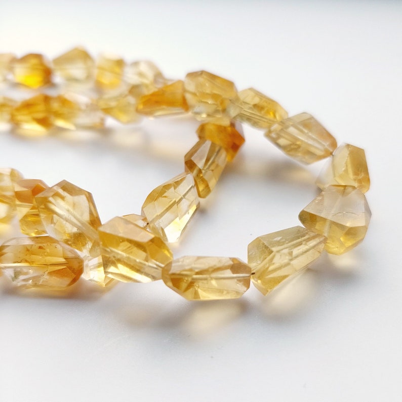 May include: A strand of faceted citrine beads in a warm yellow color. The beads are faceted and have a translucent appearance.