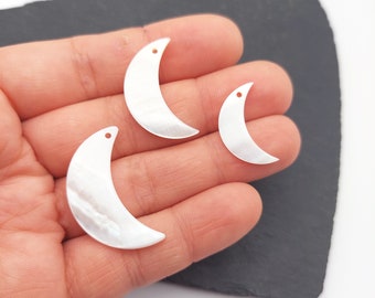 May include: Three white mother of pearl crescent moon charms with a hole for stringing. The charms are different sizes and are shown in a hand.