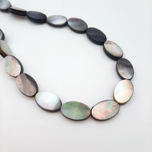 May include: A strand of oval-shaped black mother of pearl beads. The beads have an iridescent sheen and are strung on a clear thread.