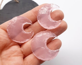 May include: Three pink crescent moon shaped pieces of polished agate. The agate is translucent and has a smooth, polished surface.