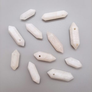 May include: Ten white, opaque, crystal-shaped pendants with a hole drilled through the center. The pendants are all different sizes and shapes, but they are all roughly the same length.