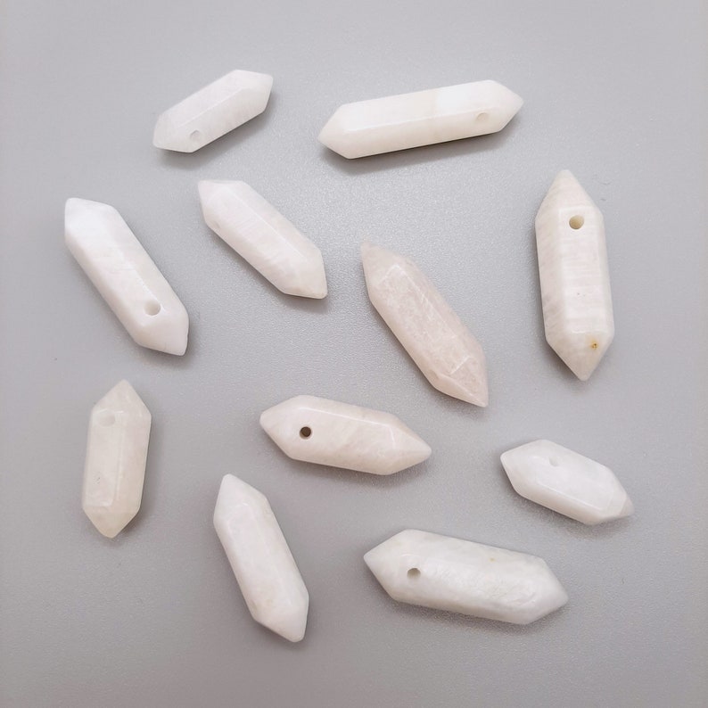 May include: Ten white, opaque, crystal-shaped pendants with a hole drilled through the center. The pendants are all different sizes and shapes, but they are all roughly the same length.