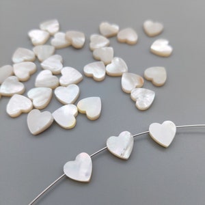 May include: A scattering of white mother of pearl heart-shaped beads, some of which are strung on a silver wire.