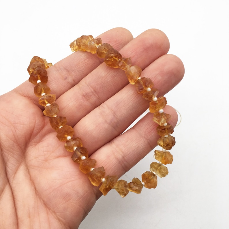 Pu&ograve; includere: Una collana di perle di pietre preziose color marrone dorato, ogni perla &egrave; sfaccettata e ha una forma irregolare e ruvida. Le perle sono infilate su un filo elastico trasparente.