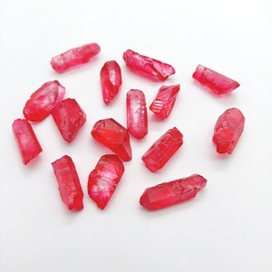 May include: A collection of 15 small, red, crystal-like points. The points are scattered on a white surface.