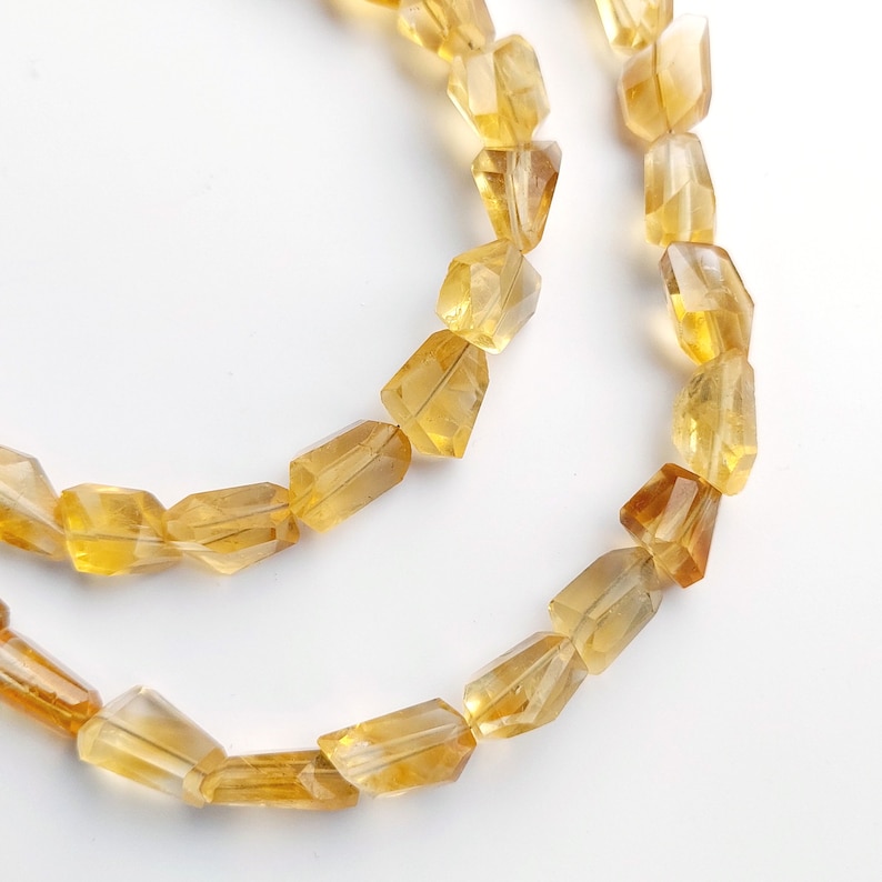 May include: A strand of faceted, golden citrine beads. The beads are all roughly the same size and shape, and they have a smooth, polished finish.