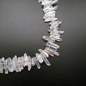 Pode incluir: Uma linha de pontas de cristal branco iridescente, tamb&eacute;m conhecidas como quartzo aura de anjo, dispostas em semic&iacute;rculo sobre um fundo preto.