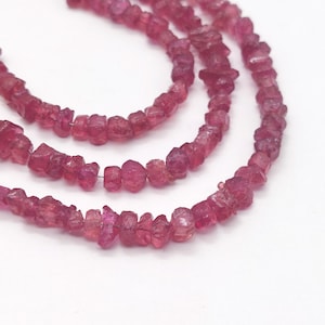 May include: A strand of pink ruby beads, each bead is a rough, irregular shape. The beads are strung on a clear thread and are arranged in a loose, flowing pattern.