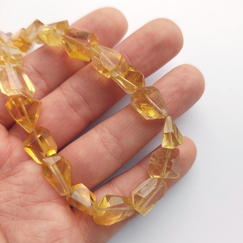 May include: A bracelet made of faceted, yellow citrine beads. The beads are strung on a clear elastic cord and are approximately 10mm in diameter.