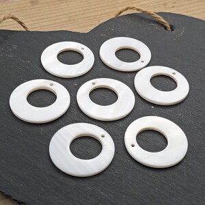 Puede incluir: Siete anillos decorativos redondos de n&aacute;car blanco con un agujero en el centro. Cada anillo tiene dos peque&ntilde;os agujeros en el borde exterior.