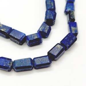 Könnte beinhalten: Eine Strang dunkelblauer Lapislazuli-Perlen mit facettierter, rechteckiger Form. Die Perlen haben einen funkelnden, metallischen Schimmer.