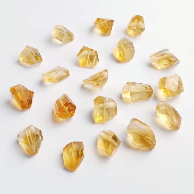 May include: A collection of 18 faceted, golden yellow citrine gemstone beads. The beads are various shapes and sizes, with some being more elongated than others. The beads are all polished and have a smooth, shiny finish.