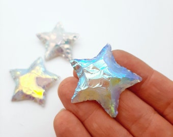 May include: Three iridescent star-shaped crystals, one held in a hand, with a blue, purple, and green color shift.