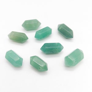 May include: Eight green gemstone beads in the shape of a pointed oval with a hole drilled through the center. The beads are scattered on a white surface.