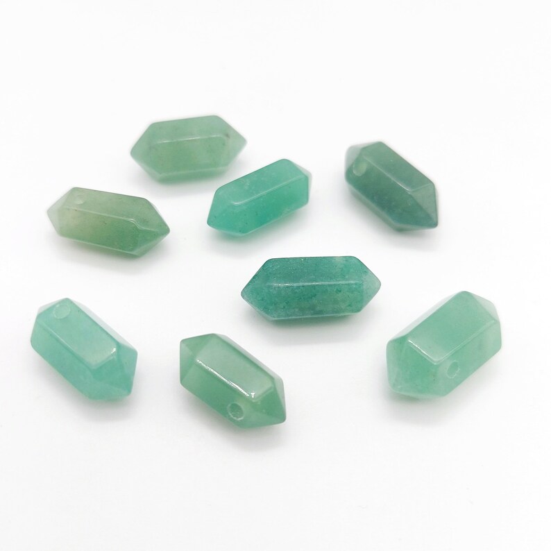 May include: Eight green gemstone beads in the shape of a pointed oval with a hole drilled through the center. The beads are scattered on a white surface.