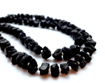 Peut inclure: Un collier de perles noires en pierres brutes naturelles. Le collier est composé de nombreuses petites perles de forme irrégulière.