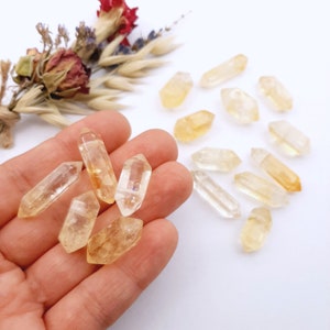 May include: A collection of yellow citrine crystal points, some are in a hand, others are scattered on a white surface.