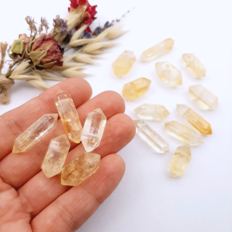 May include: A collection of yellow citrine crystal points, some are in a hand, others are scattered on a white surface.