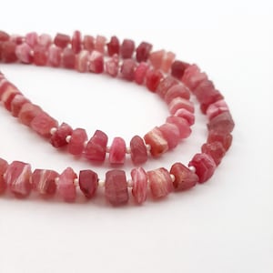 May include: A strand of pink and white gemstone beads. The beads are faceted and have a slightly irregular shape. The beads are strung on a clear thread.