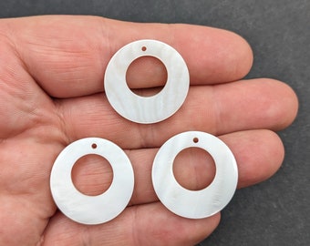 May include: Three white mother of pearl round circles with a hole in the center. The circles are approximately 2 inches in diameter.