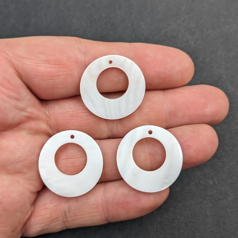 Puede incluir: Tres c&iacute;rculos redondos de madreperla blanca con un agujero en el centro. Los c&iacute;rculos tienen un di&aacute;metro de aproximadamente 5 cm.