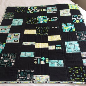 May include: A black and white patchwork quilt with green and blue accents. The quilt features a variety of text and symbols related to video games, including the words "Play", "Level", "Go!" and "Next".
