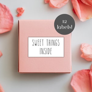 May include: A pink box with a white label that says "Sweet Things Inside". The box is surrounded by pink rose petals. A gray circle with white text says "12 labels!"