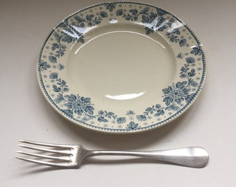 May include: A white ceramic plate with a blue floral pattern. The plate is empty and a silver fork is placed below it.