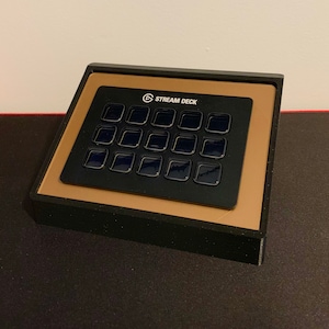 May include: A black Stream Deck with 15 customizable buttons. The buttons are arranged in a 5x3 grid and have a black background with a white border. The Stream Deck is a popular tool for streamers and content creators.