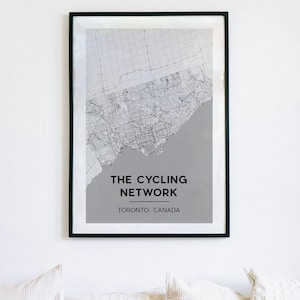 May include: A framed print featuring a map of Toronto's cycling network. The map is in grayscale, with a black frame. The text "THE CYCLING NETWORK" and "TORONTO, CANADA" are displayed in black font.