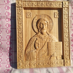 May include: A carved wooden icon of Jesus Christ holding a book. The icon is framed with intricate carvings and has a halo around Jesus' head.