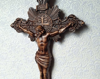 May include: A wooden crucifix with a dark brown finish. The figure of Jesus Christ is carved in detail and has a crown of thorns. The cross features a decorative INRI inscription and a circular design with the words "Pax" and "INRI".