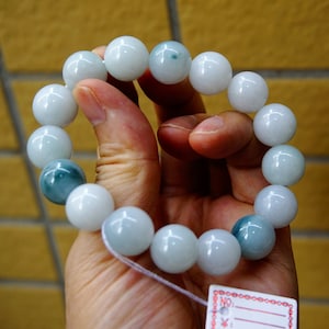 May include: A jade bracelet with light blue and white beads. The bracelet is made of 14 beads and is strung on a white cord.