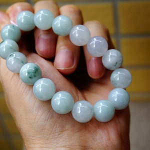 May include: A jade bracelet with light green and white beads. The bracelet is made of round beads and is strung on a clear elastic cord.