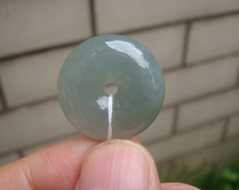 May include: A light green jade pendant in the shape of a donut with a hole in the center. The pendant is smooth and polished.