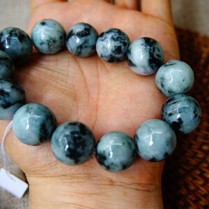 May include: A jade bracelet with black and green marbling. The bracelet is made of round beads and is strung on a white cord.