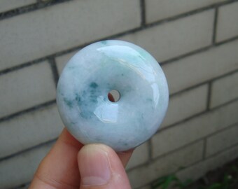 May include: A light green jade pendant in the shape of a donut with a hole in the center. The pendant is smooth and polished.