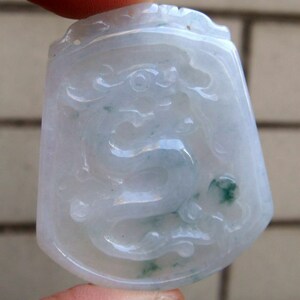 以下が含まれることがあります： 白翡翠のペンダントで、龍の彫刻が施されています。龍は薄い緑色で、ペンダントは滑らかで磨かれた仕上げになっています。