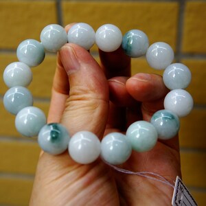May include: A jade bracelet featuring light green and white beads. The bracelet is crafted from natural jade and has a smooth, polished finish.