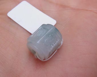 Puede incluir: Un anillo de jade tallado translúcido, con un tono verde claro. El anillo presenta intrincadas tallas y está asegurado con un hilo blanco fino. Una etiqueta blanca en blanco es visible en el fondo.