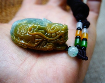May include: A jade green and yellow dragon pendant carved from jade, hanging on a black cord with green and orange beads.