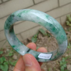 May include: A jade bangle bracelet with a white and green color scheme. The bangle is polished and has a smooth surface.
