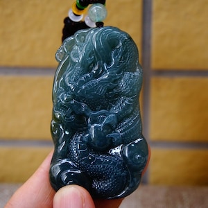 May include: A jade pendant carved with a detailed dragon design. The pendant is a deep blue-green color and has a glossy finish.