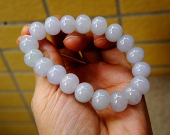 Könnte beinhalten: Ein Armband aus helllavendelfarbenen Jadeperlen. Die Perlen sind rund und glatt, und das Armband ist auf einer durchsichtigen Gummikordel aufgefädelt.