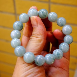May include: A light blue beaded bracelet with large, round beads. The bracelet is held in a hand, showcasing the smooth, polished surface of the beads. The beads have a subtle, natural variation in colour.