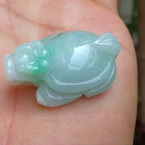 May include: A jade turtle figurine, carved with intricate details. The turtle is a pale green colour with darker green accents. The figurine is smooth and polished, with a glossy finish. The turtle's head and legs are visible, and the shell is well-defined.